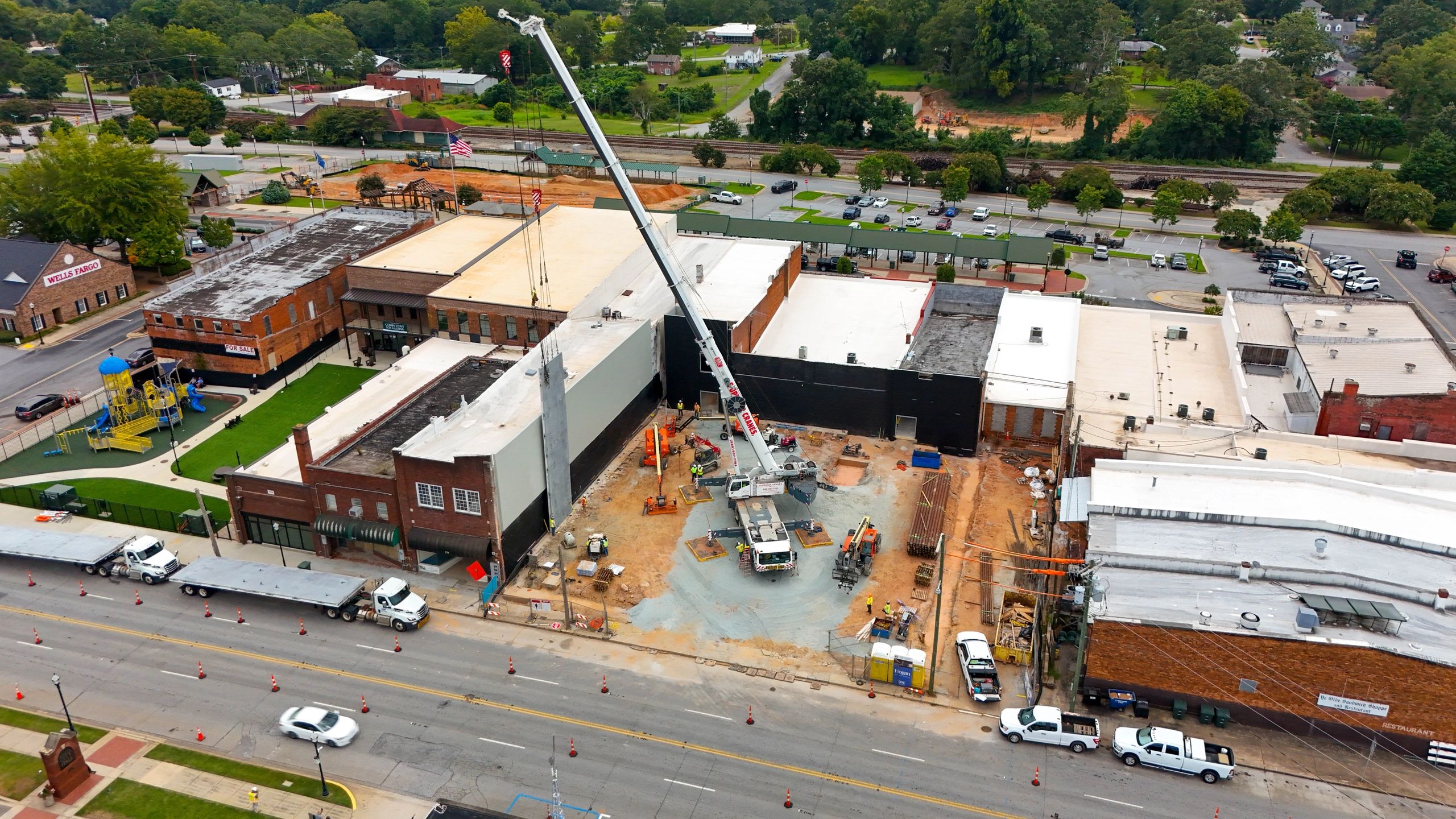 Aerial view of a crane and crews installing concrete wall panels between downtown buildings.