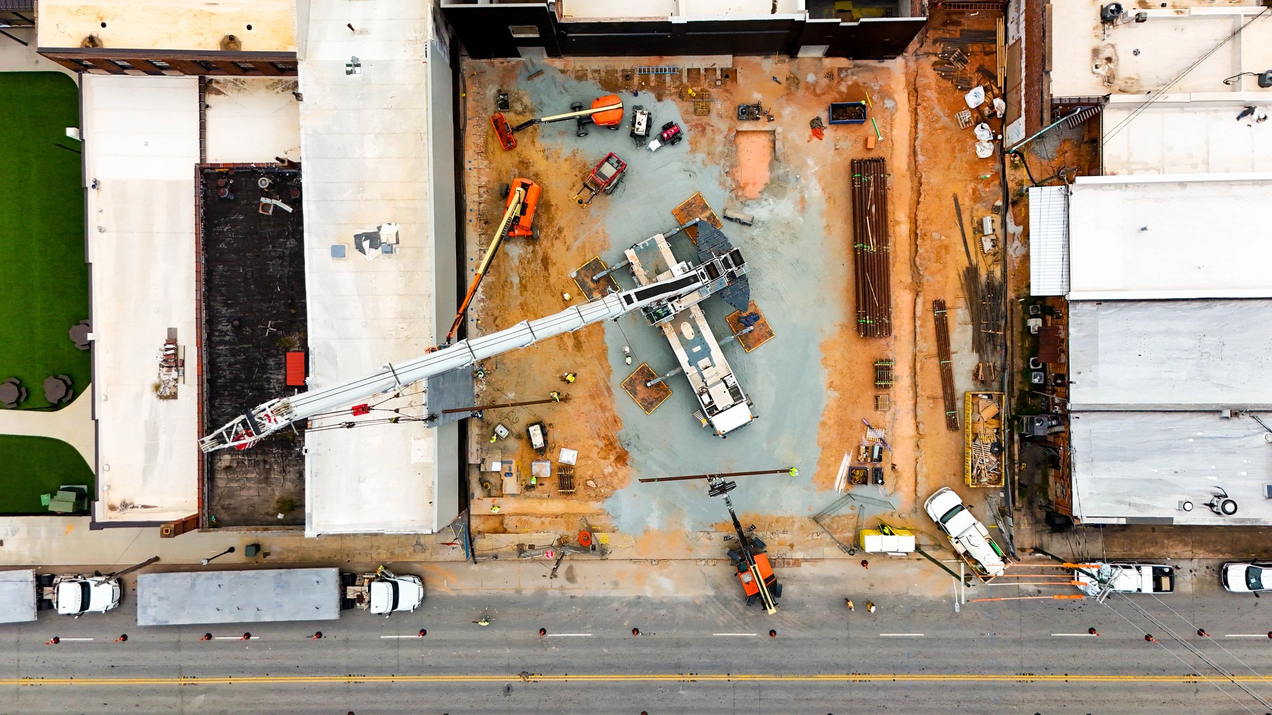 Overhead view of a crane, boom lifts, workers, and staged materials at a downtown construction site.