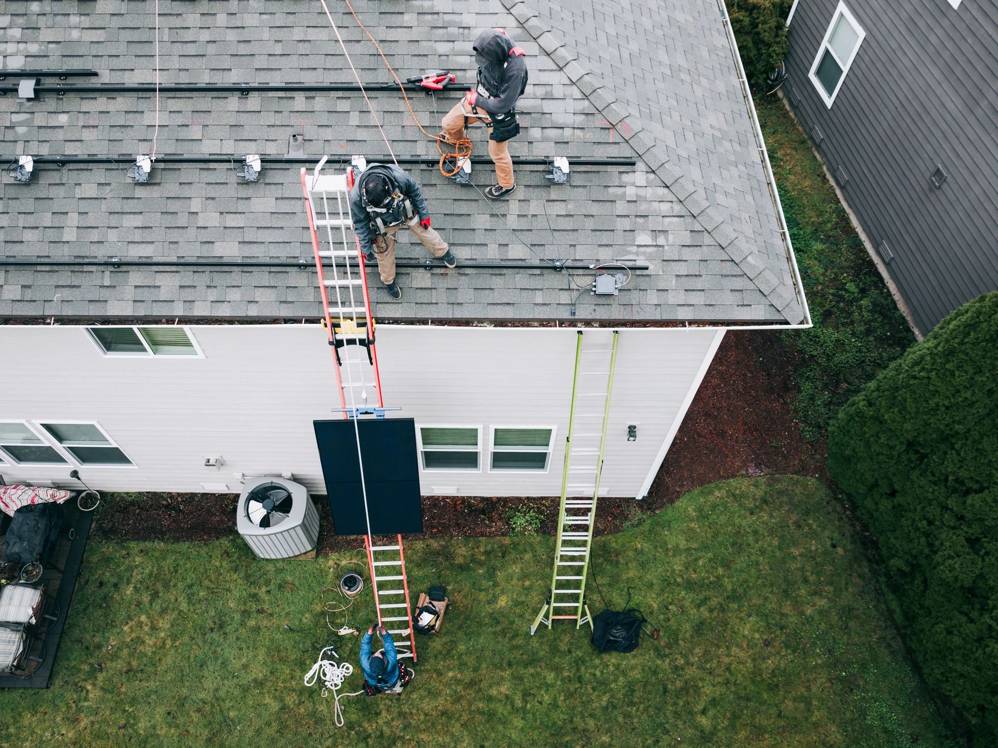 Overhead view of workers installing solar panel mounting rails on a house roof.
