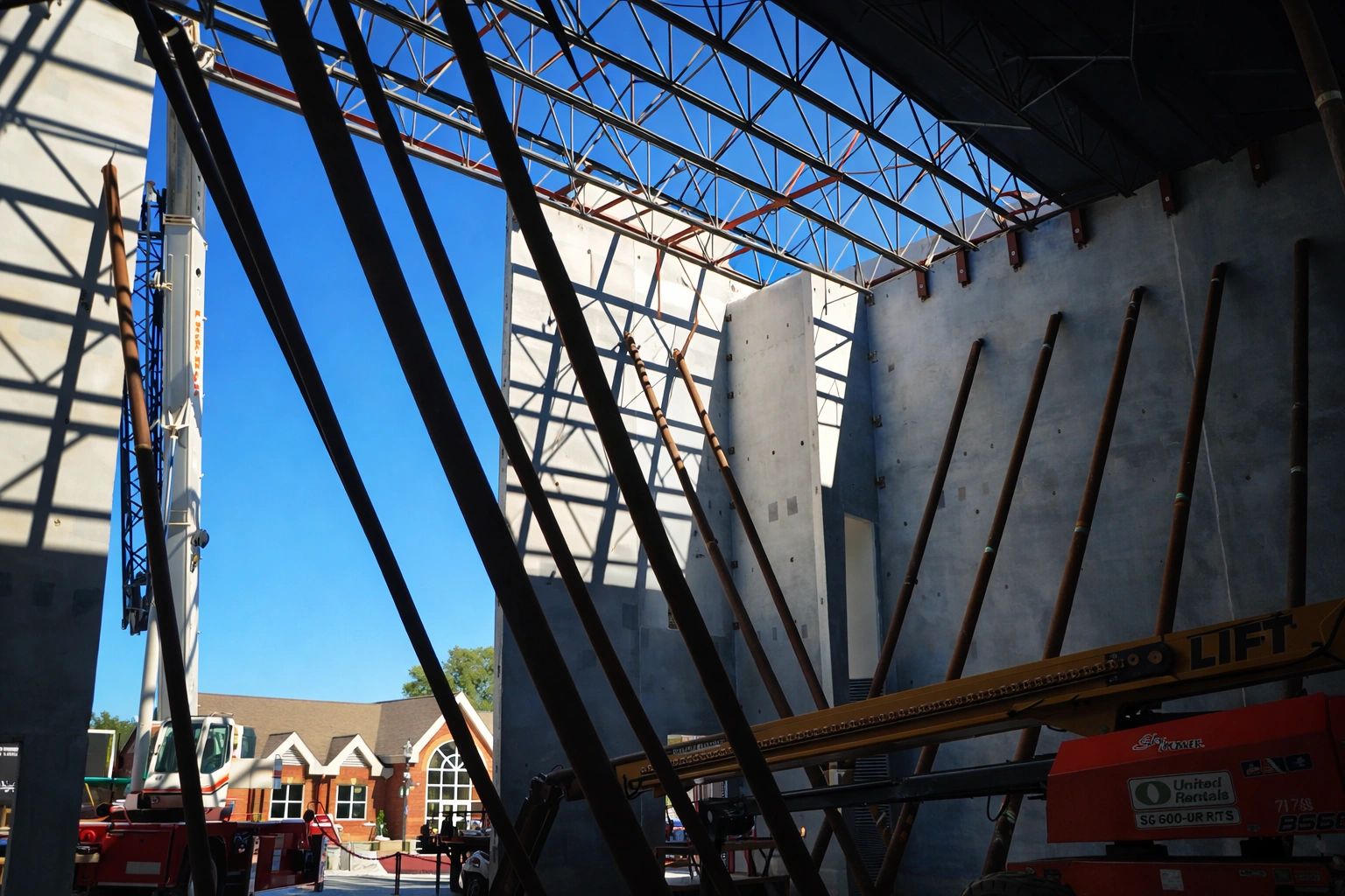 Interior construction view of concrete walls, temporary braces, and exposed steel roof trusses.