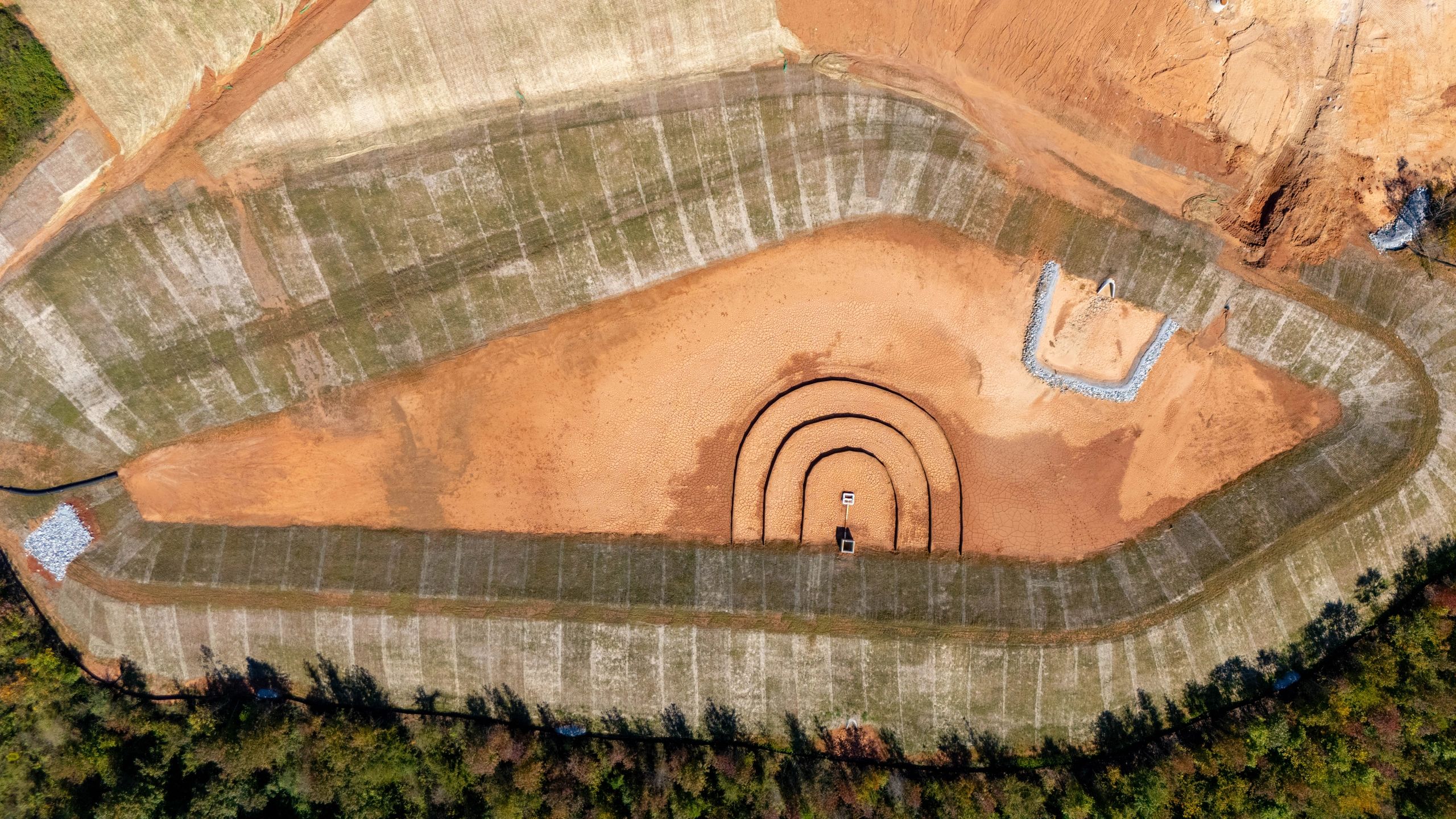 Overhead view of a dry stormwater basin with grassed slopes and drainage structures.